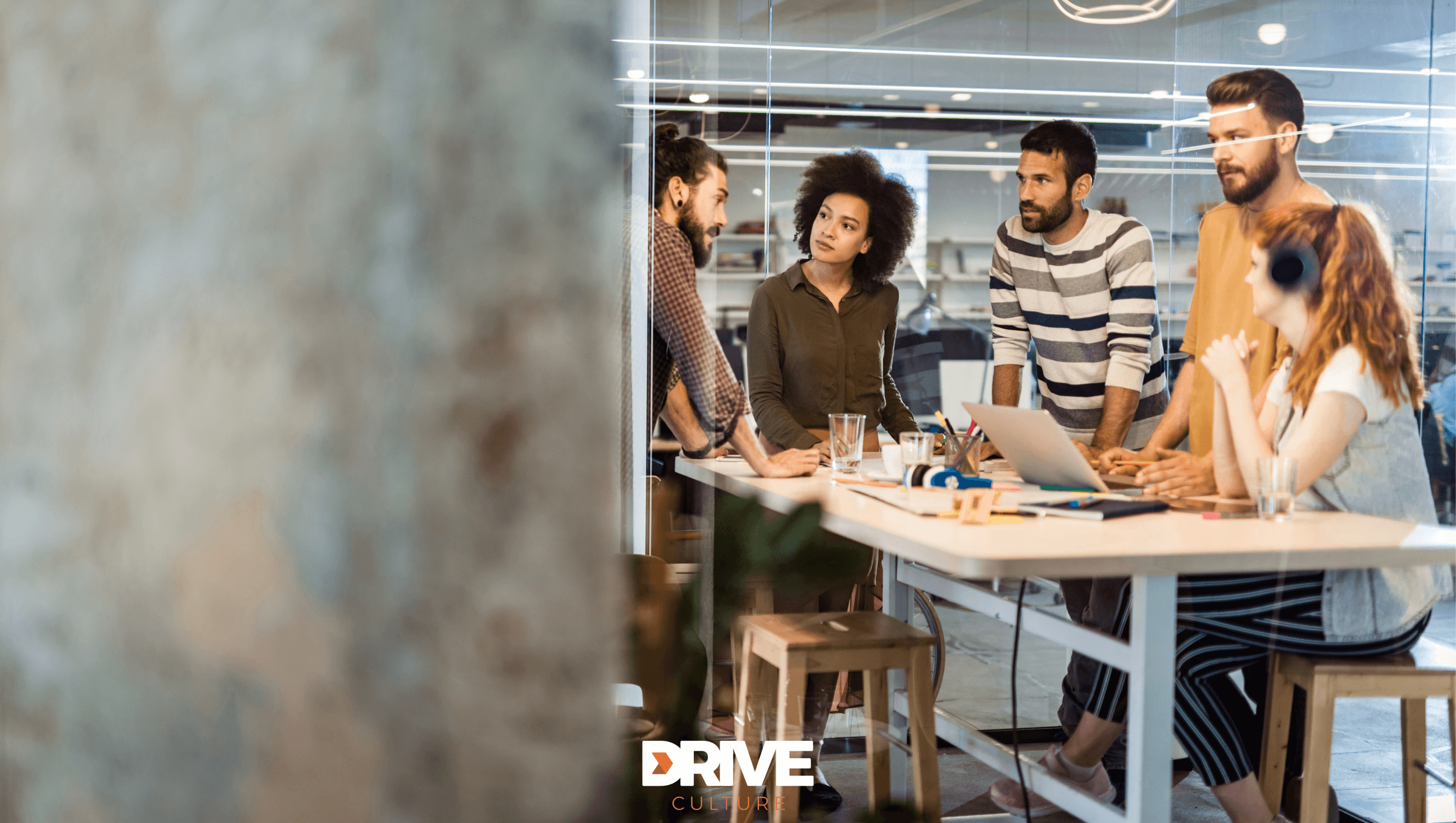 Team collaborating around a high table in a bright modern office, representing workplace culture and teamwork.