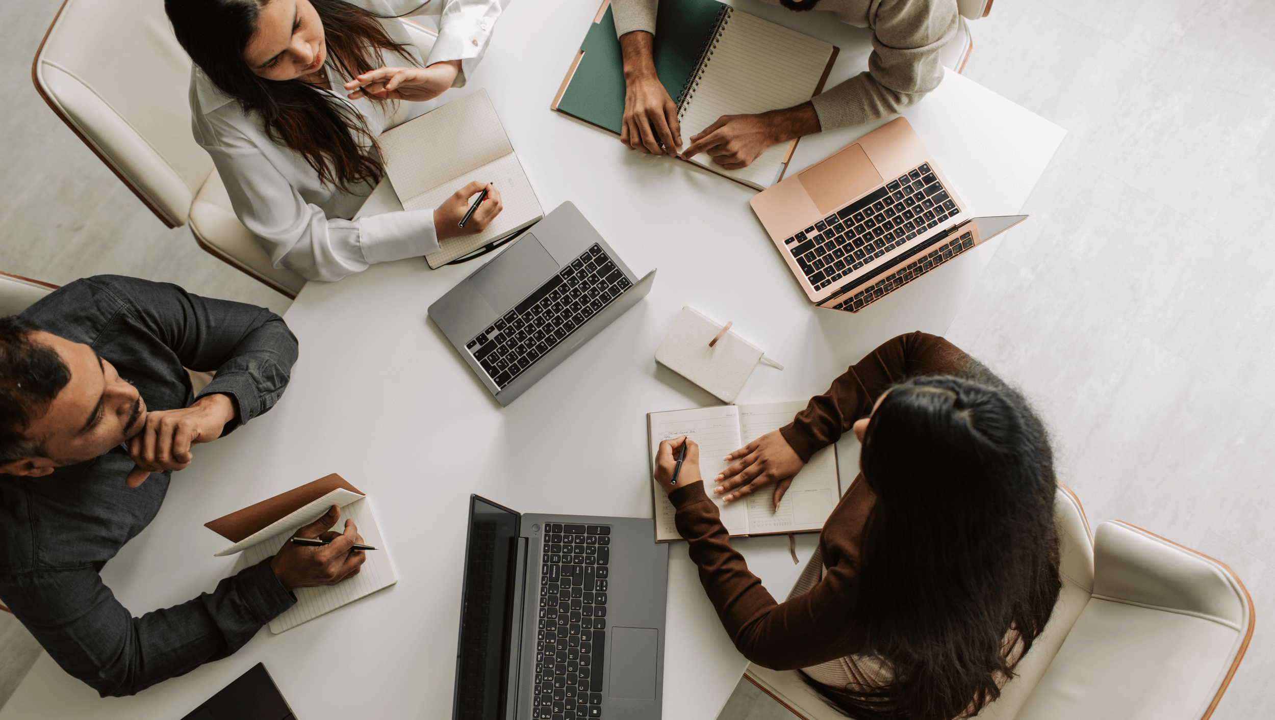 Small business team in New Zealand collaborating around a table with laptops, representing effective HR services and teamwork.